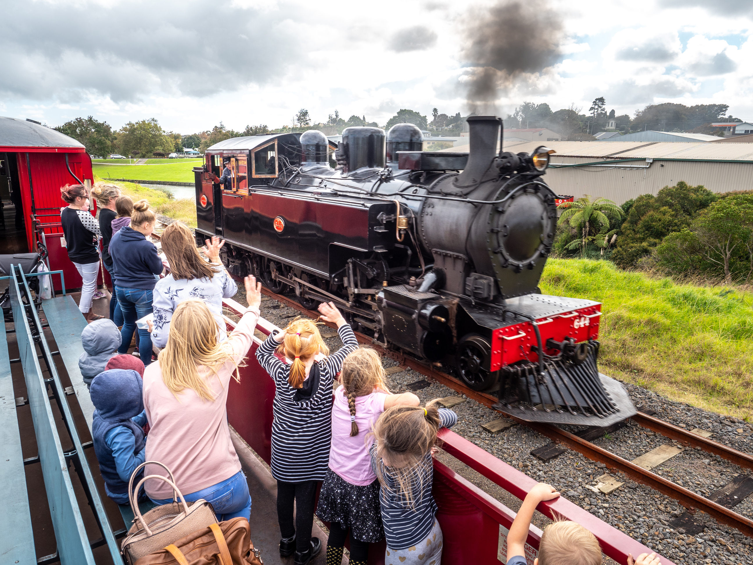 Steam locomotive passing passengers aboard an open-air carriage at Glenbrook Vintage Railway